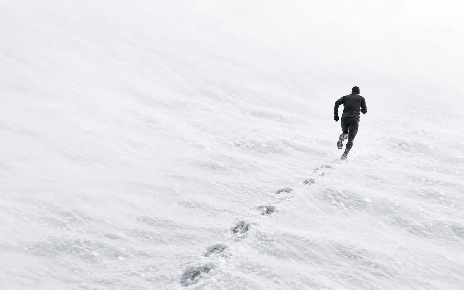 A man running away into a white winter landscape, leaving a trail of footprints in the snow.