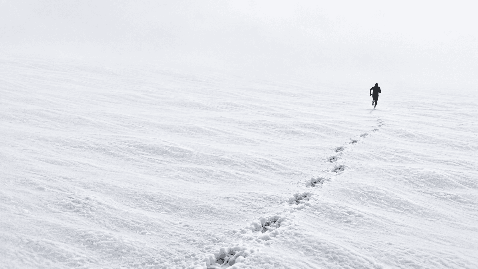The runner continues into a quiet white landscape with a long trail of footprints behind him.